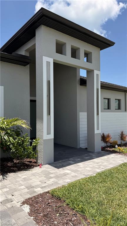 Modern exterior entrance featuring a large overhang, decorative square cutouts, stucco finish, and integrated vertical lighting fixtures
