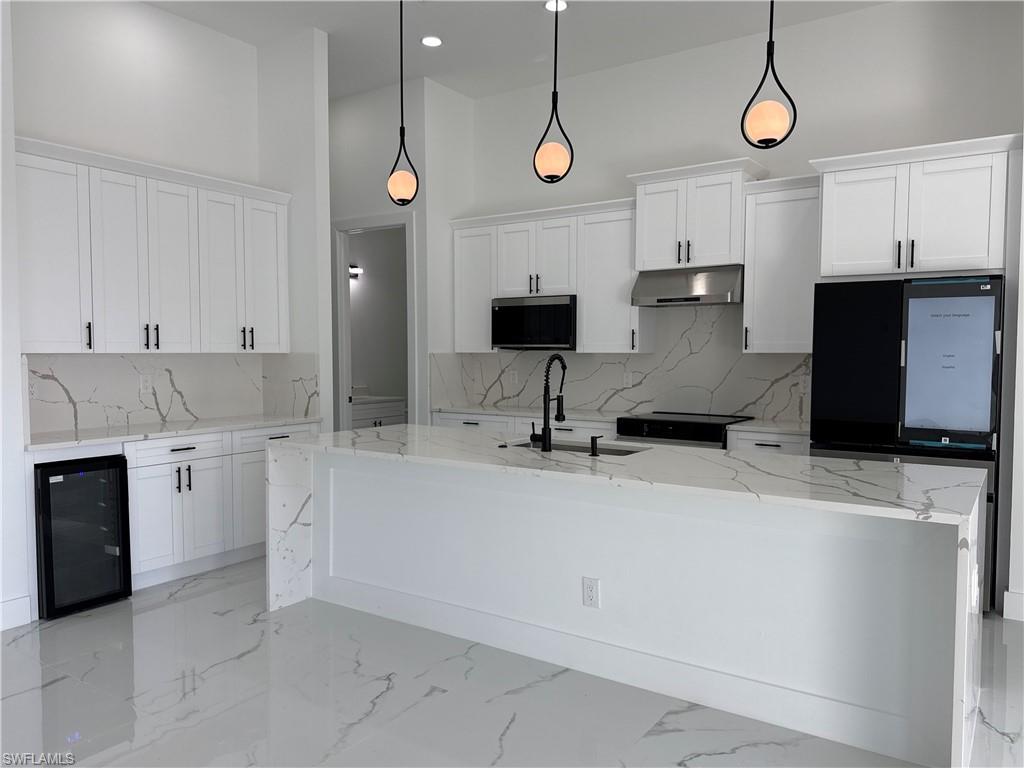 Contemporary kitchen featuring an expansive island with a waterfall edge, white shaker-style cabinetry, integrated stainless steel appliances, and sleek pendant lighting