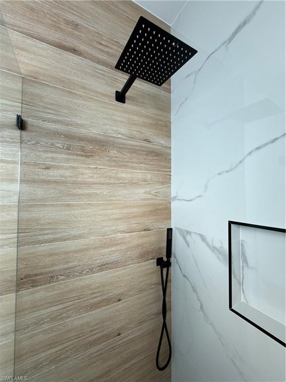 Rainfall showerhead with matte black finish, handheld shower spray, wood-finish wall tiling, large format marble-look wall tiles, and a recessed shower niche with black trim