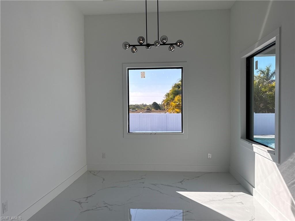 Modern chandelier with glass globes, large format porcelain tile flooring, contemporary window trim, and a white privacy fence