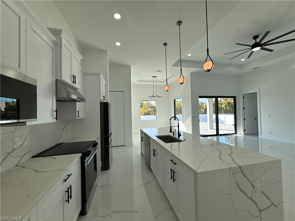 Modern kitchen featuring white cabinetry with black hardware, white countertops and backsplash, stainless steel appliances, and a large center island with an integrated sink