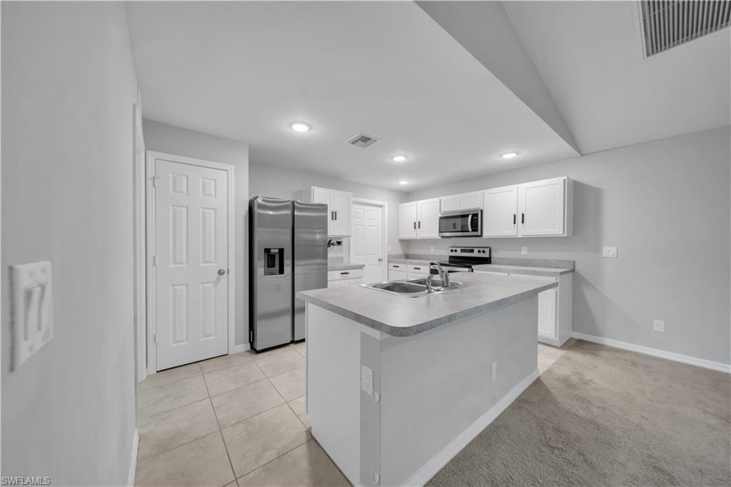 Kitchen featuring white cabinetry, stainless steel appliances, an island with an integrated sink, and recessed lighting