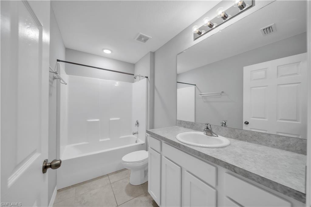 Bathroom featuring a white vanity with a single sink, an integrated shower/tub combination, a large wall-mounted mirror, and tile flooring