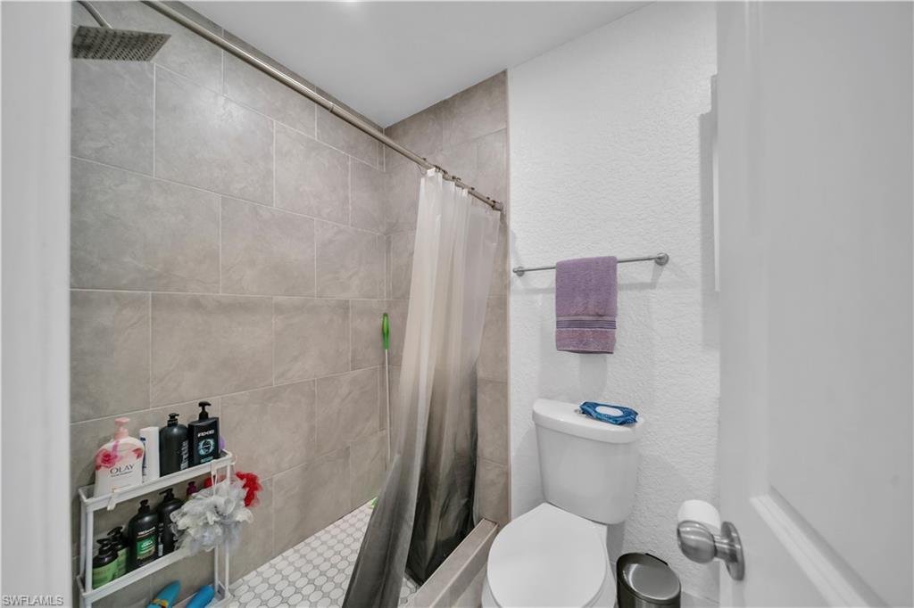 Shower with gray tile surround, rainfall showerhead, and white hexagonal tile flooring