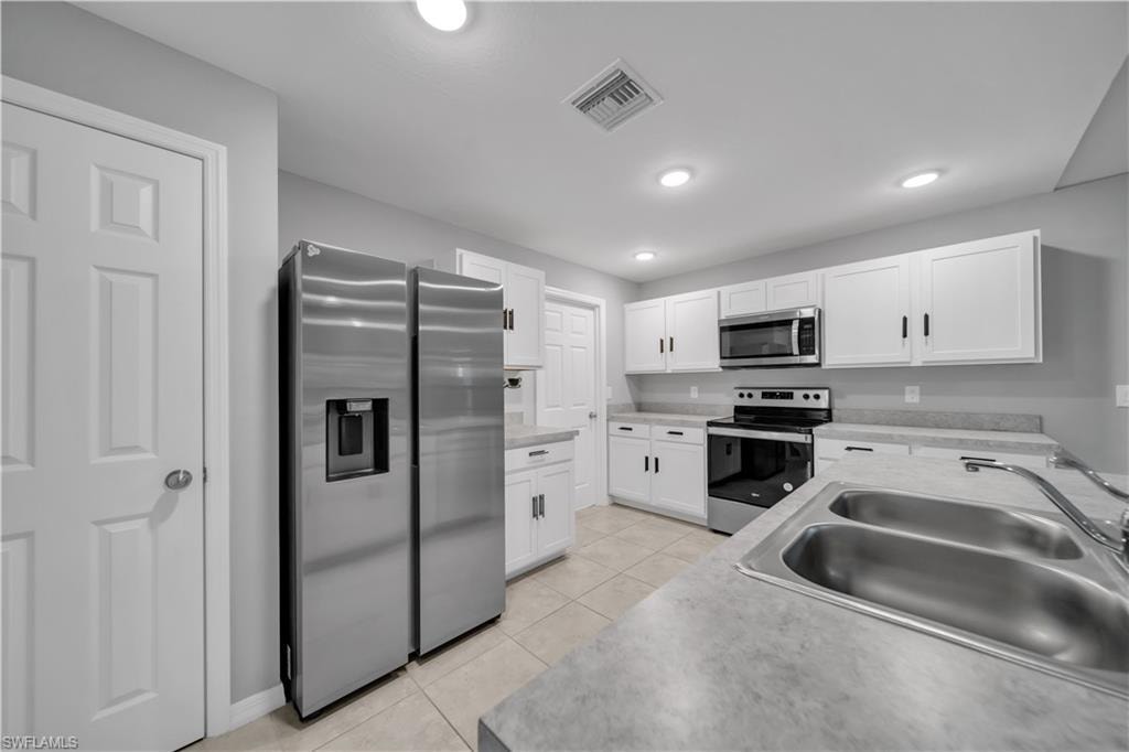 Kitchen featuring white cabinetry, stainless steel appliances, a dual basin sink, and tile flooring