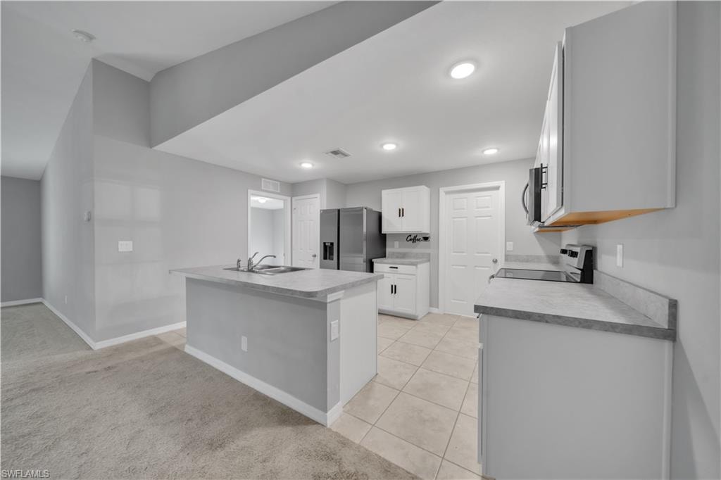 Open-concept kitchen featuring an island with an integrated sink, white cabinetry, and recessed lighting