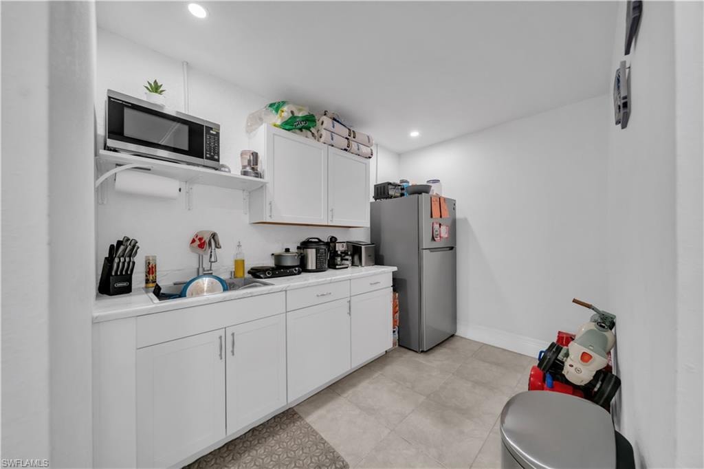 Modern kitchen featuring white cabinetry with ample storage, stainless steel refrigerator, built-in microwave, and tile flooring throughout
