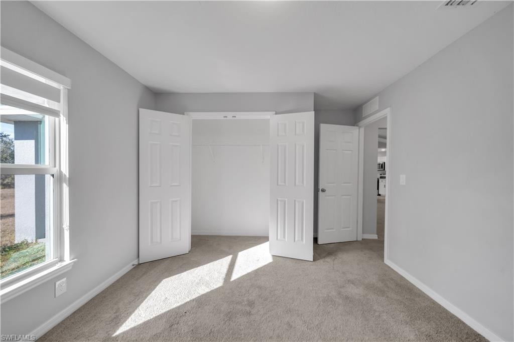Light gray painted walls with carpet flooring, a multi-pane window, and a bi-fold closet door