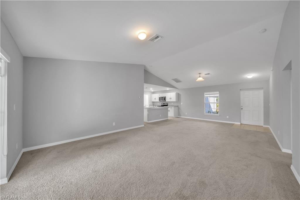 Open-concept living area with vaulted ceilings, light gray walls, and carpet flooring