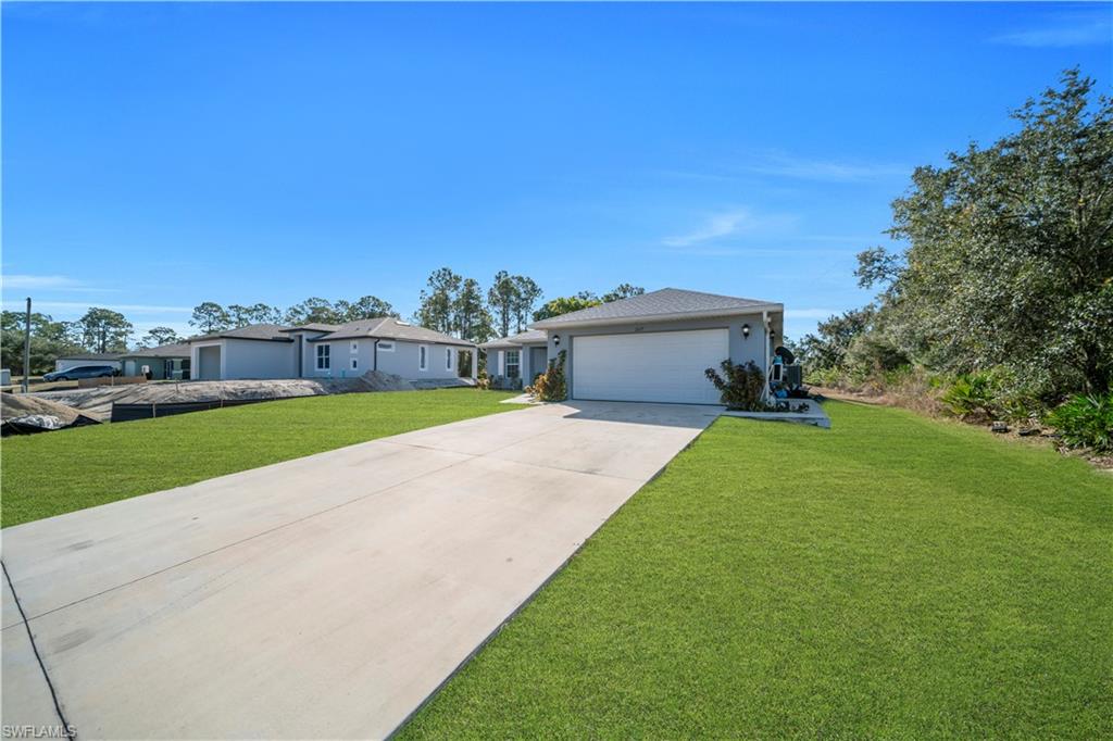 Expansive grounds featuring a manicured lawn with mature landscaping and established trees, complemented by a long concrete driveway leading to an attached two-car garage