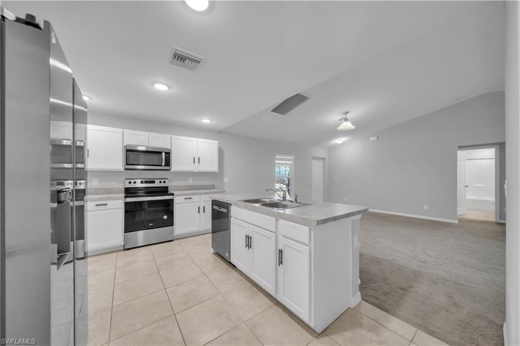 Kitchen featuring white cabinetry, stainless steel appliances, an island with an integrated sink, tile flooring, and recessed lighting