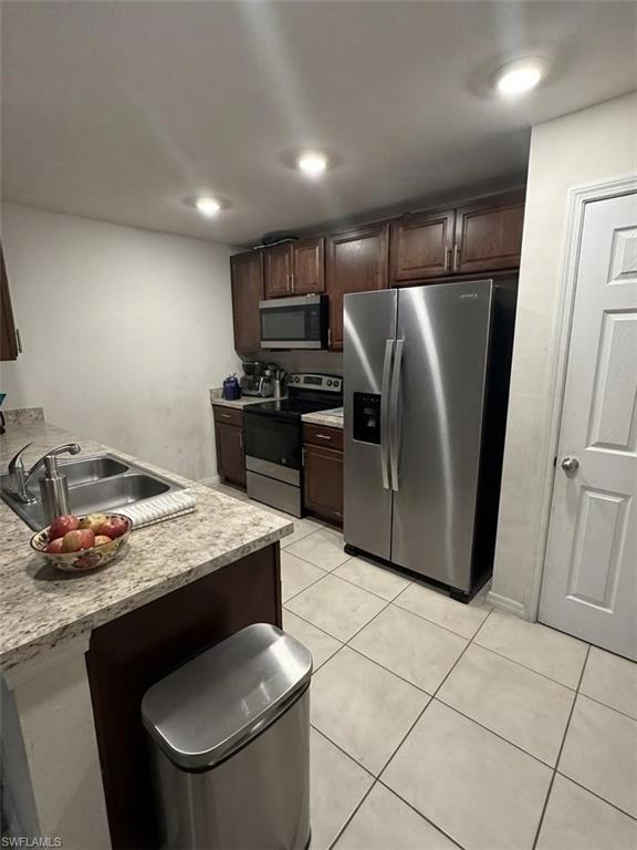Kitchen featuring wood cabinetry, light-toned tiled flooring, stainless steel appliances, and recessed lighting
