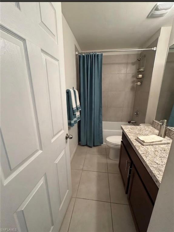 Bathroom with tile flooring, a dark wood-finish vanity with a light-toned countertop, a built-in tub with wall tile surround, and a chrome shower fixture