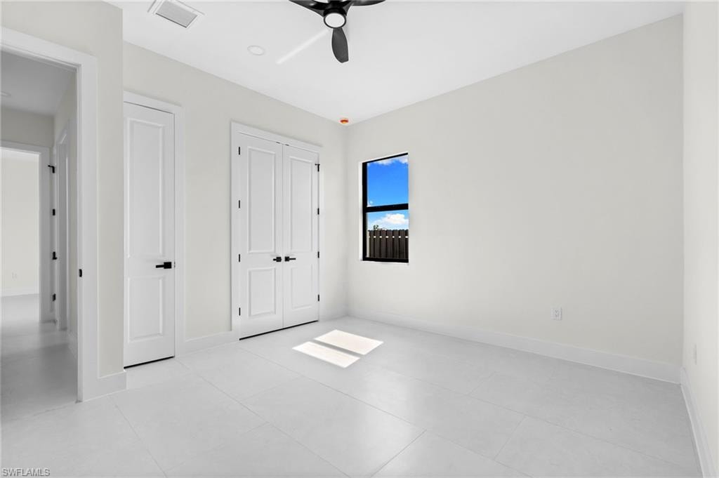 White tiled flooring, dual panel doors with matte black hardware, single window with dark frame, white walls, and a black ceiling fan