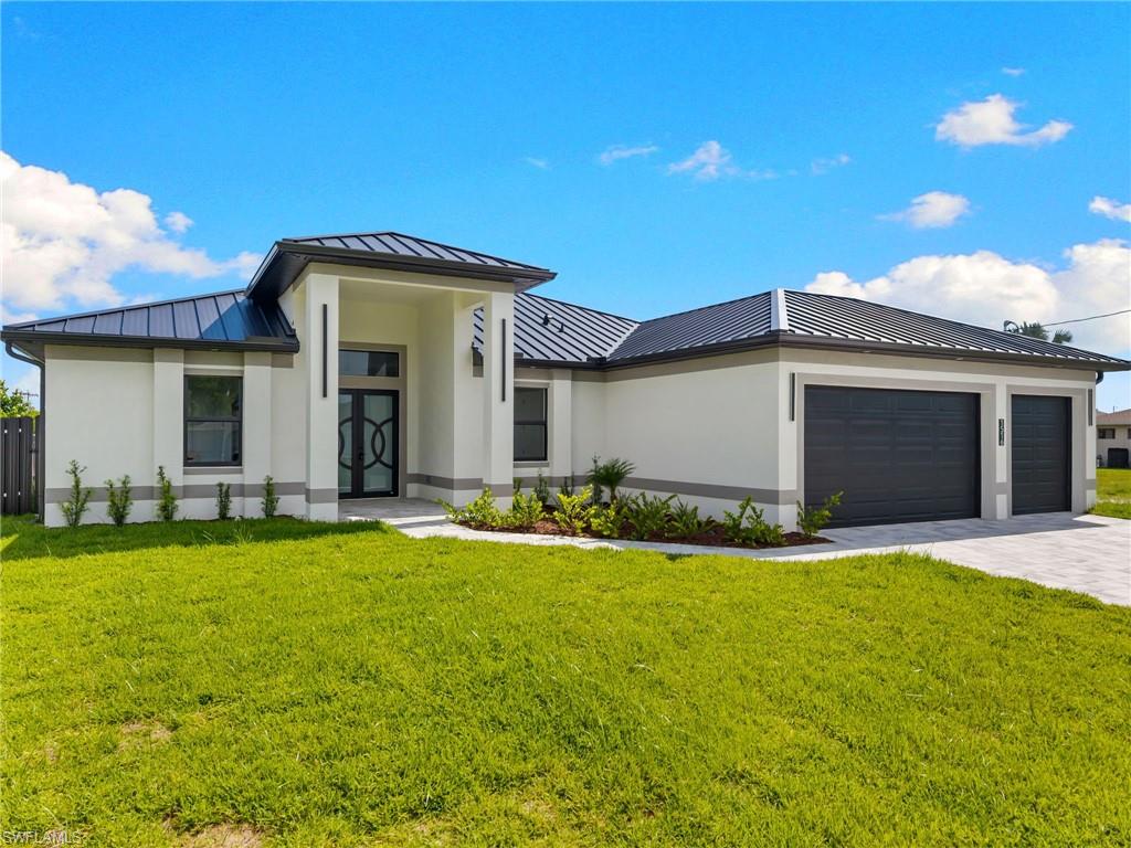 Contemporary stucco exterior with a dark metal roof, decorative front entry door, two-car garage, and paver driveway
