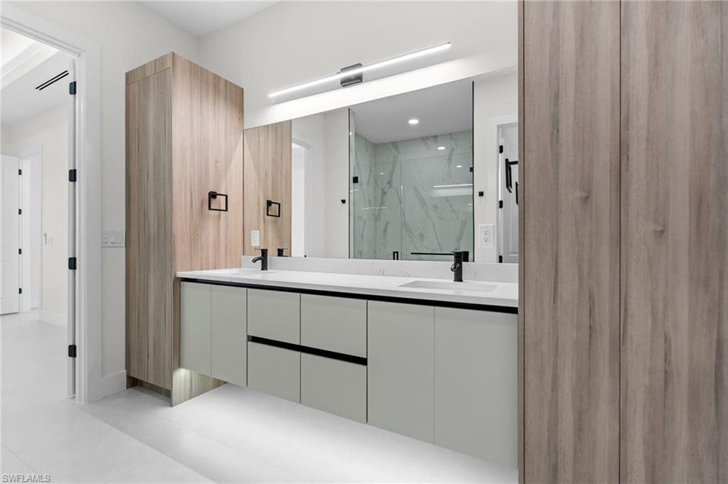 Dual vanity with white countertop, matte black fixtures, integrated sinks, and wall-mounted light bar