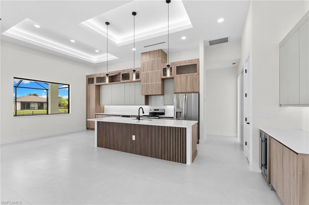 Recessed and tray ceiling lighting, stainless steel appliances, wood-finish cabinetry, and a kitchen island with a slatted wood-finish base
