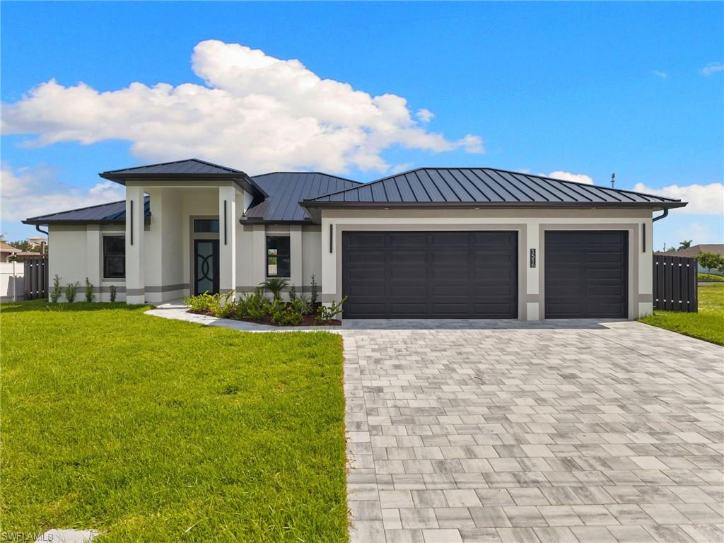 Contemporary stucco exterior with a dark metal roof, paver driveway, two-car garage, and a covered entry
