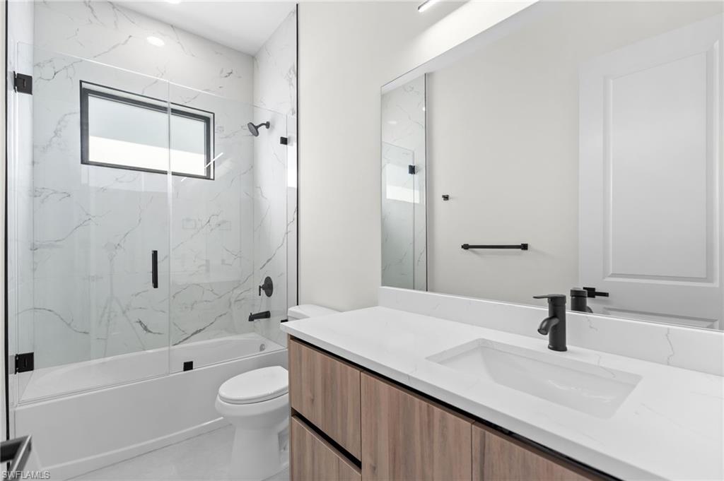 Bathtub with glass enclosure and black-framed window, complemented by a wood-finish vanity with an integrated sink and matte black fixtures