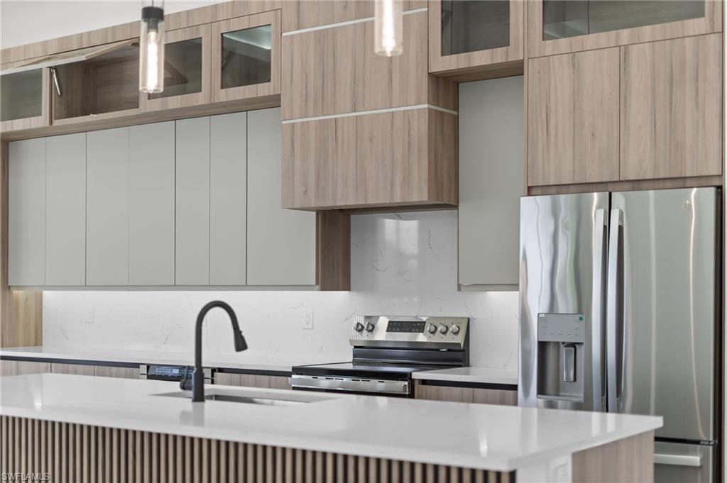 Kitchen featuring two-tone cabinetry with wood-finish and light gray doors, white countertops, a matte black gooseneck faucet, and stainless steel appliances