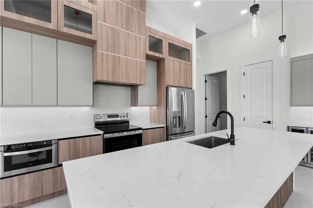 Kitchen featuring a large island with an undermount sink, a stainless steel refrigerator, built-in microwave, and wood-finish cabinetry