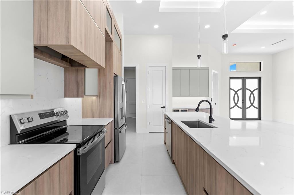 Sleek kitchen featuring wood-finish cabinetry, white countertops, built-in stainless steel appliances, and a central island with an integrated sink