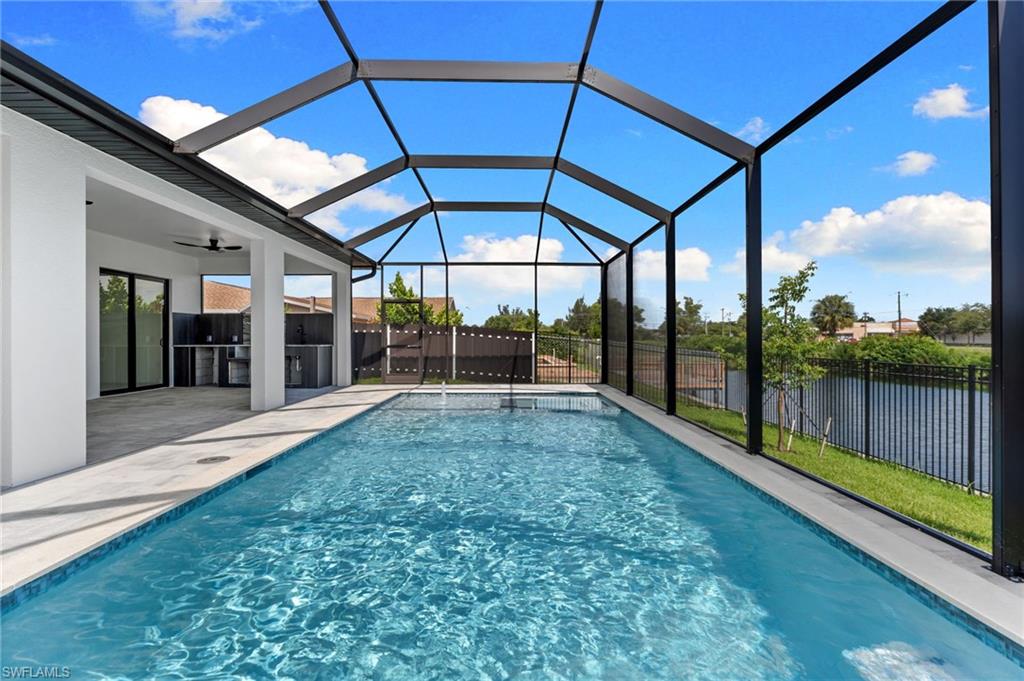 Screened-in outdoor pool area featuring a rectangular pool, a covered patio, an outdoor kitchen with built-in cabinetry, sliding glass doors, and a decorative metal fence