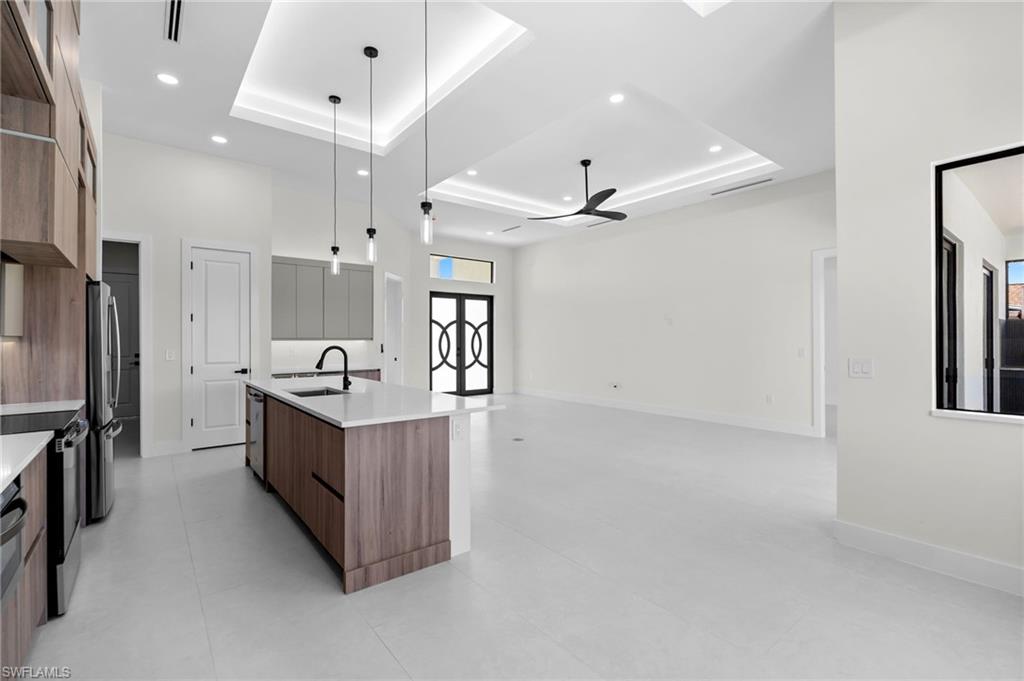 Open-concept living area featuring a large kitchen island with a white countertop, wood-finish cabinetry, stainless steel appliances, and a tray ceiling with recessed lighting
