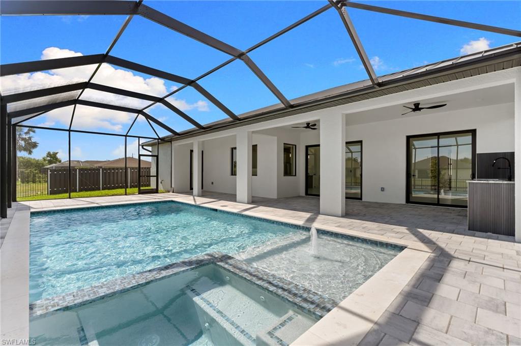 Screened outdoor living area featuring a rectangular pool, integrated spa, and a built-in outdoor kitchen