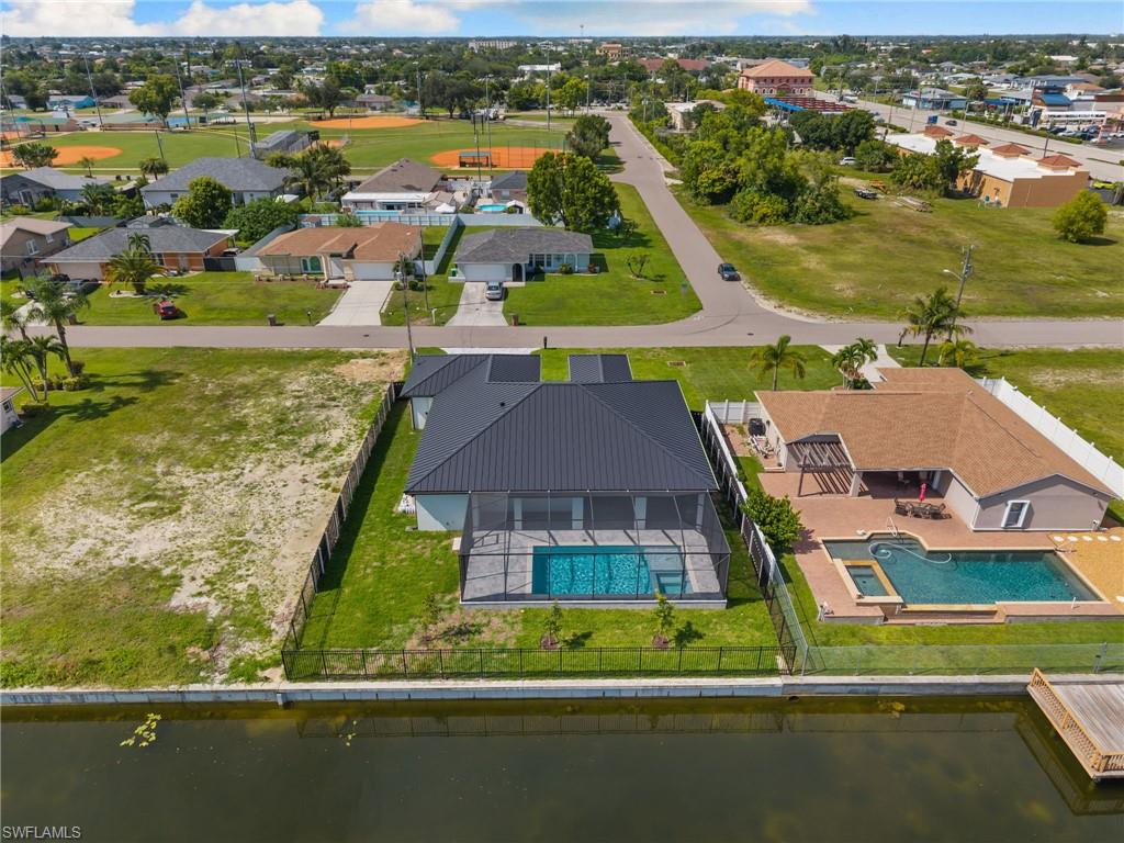 Waterfront property featuring a screened-in pool enclosure, dark metal roof, and an adjacent undeveloped lot