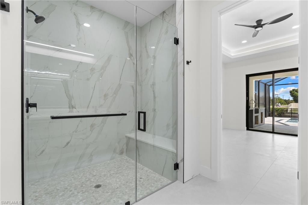 Glass-enclosed shower with a built-in bench, marble-patterned wall tile, and matte black fixtures