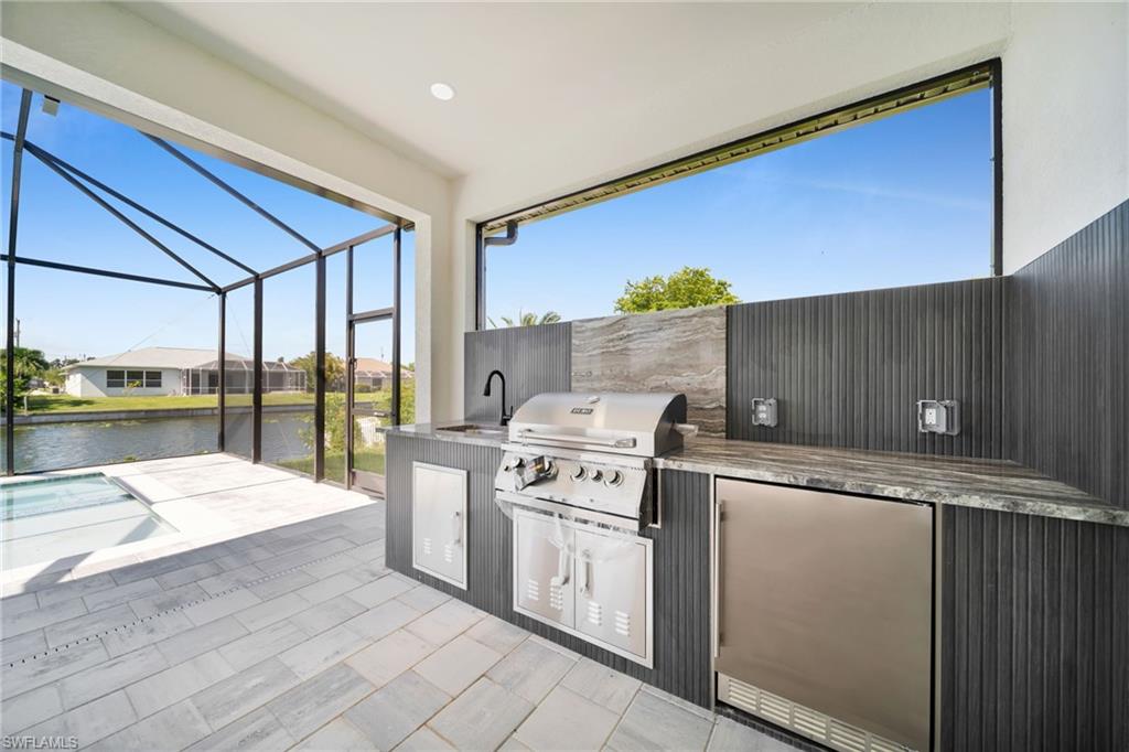 Outdoor kitchen featuring a built-in grill, sink, and under-counter refrigerator