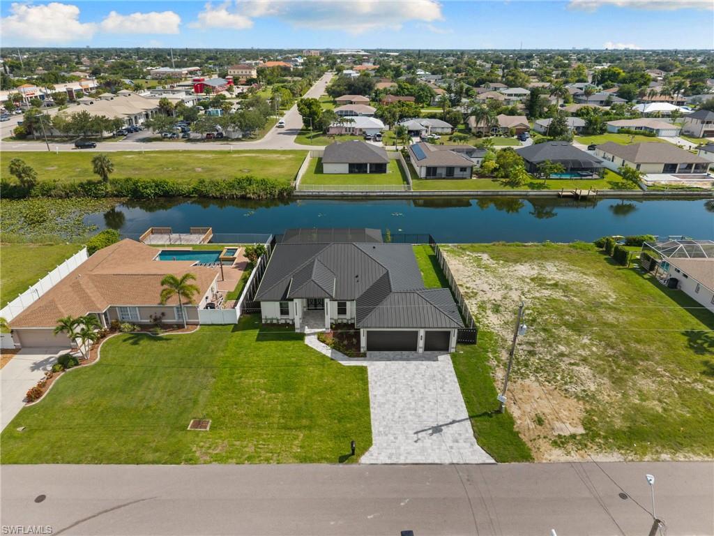 Waterfront property featuring a newly constructed residence, expansive paved driveway, and lush green lawn