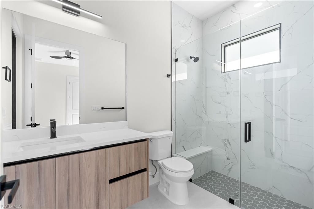Spacious bathroom featuring a frameless glass shower enclosure, wood-finish vanity with an integrated sink, and large format mirror