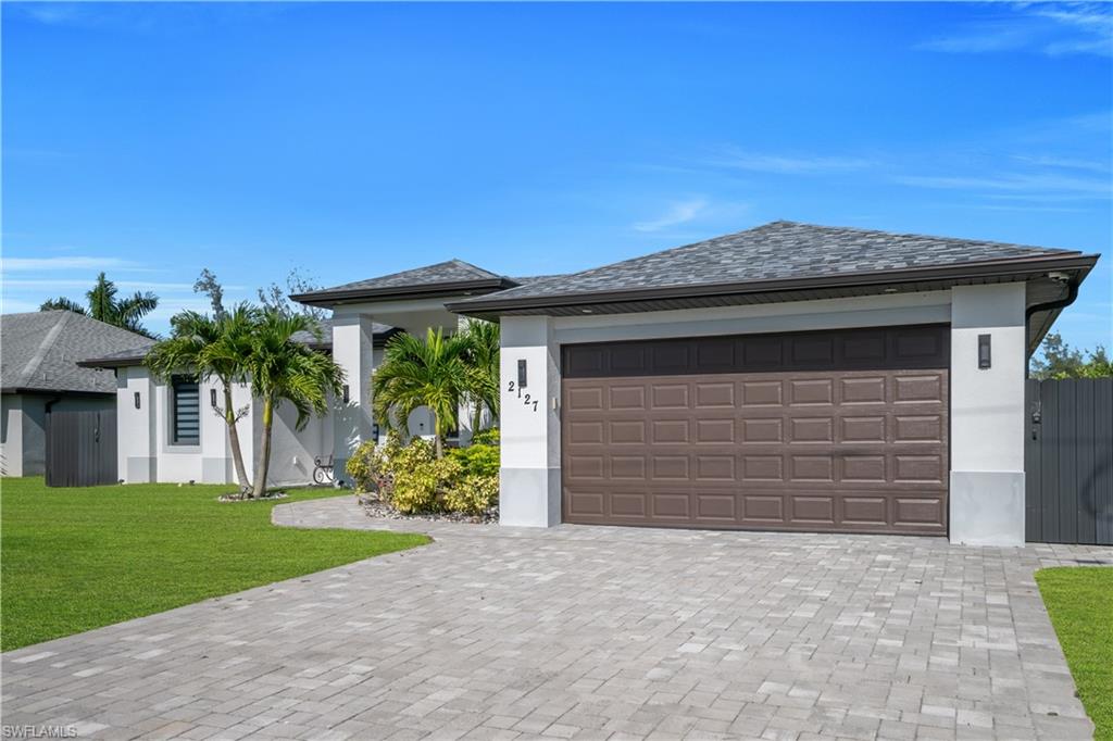 Modern stucco exterior with a brown panel garage door, paver driveway, and a shingle roof