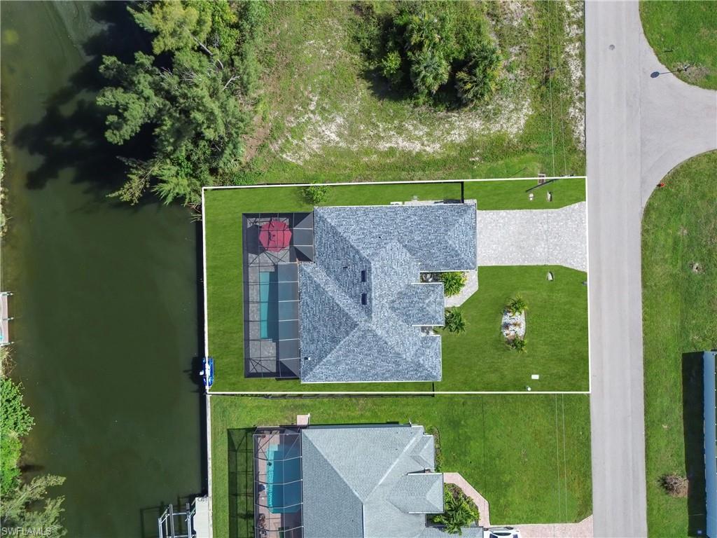 Waterfront property featuring a screened-in pool, shingle roof, paved driveway, and manicured lawn