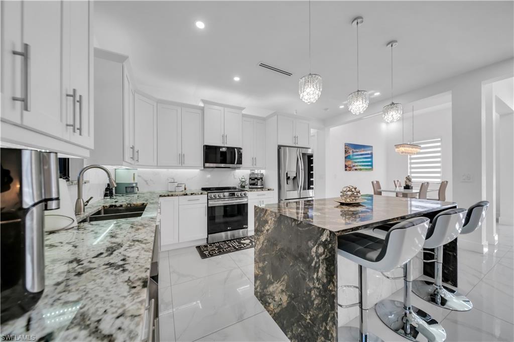 White cabinetry with stainless steel hardware, white stone-finish countertops, and a waterfall-edge kitchen island