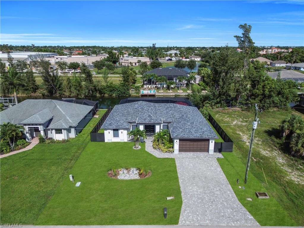 Paver driveway leading to an attached garage, white exterior, dark gray shingle roof, and lush green lawn