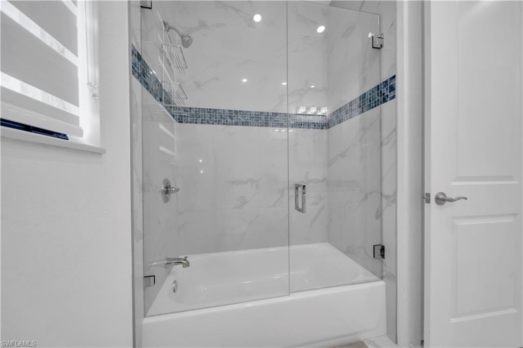 Bathtub and shower combination with clear glass enclosure, tiled surround featuring a decorative mosaic accent, and polished chrome fixtures