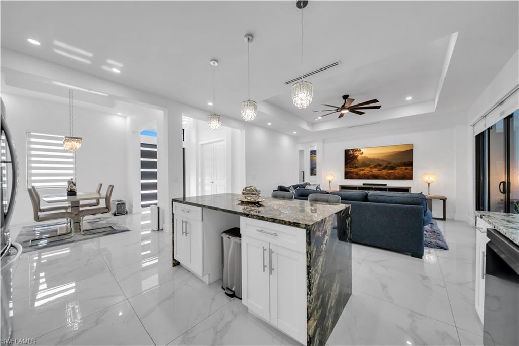Open-concept living space with large format tile flooring, a kitchen island featuring a waterfall countertop, recessed lighting, and a tray ceiling
