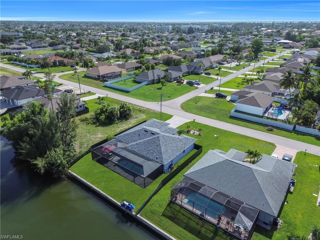 Waterfront property featuring a screened-in pool, manicured lawn, and paved driveway