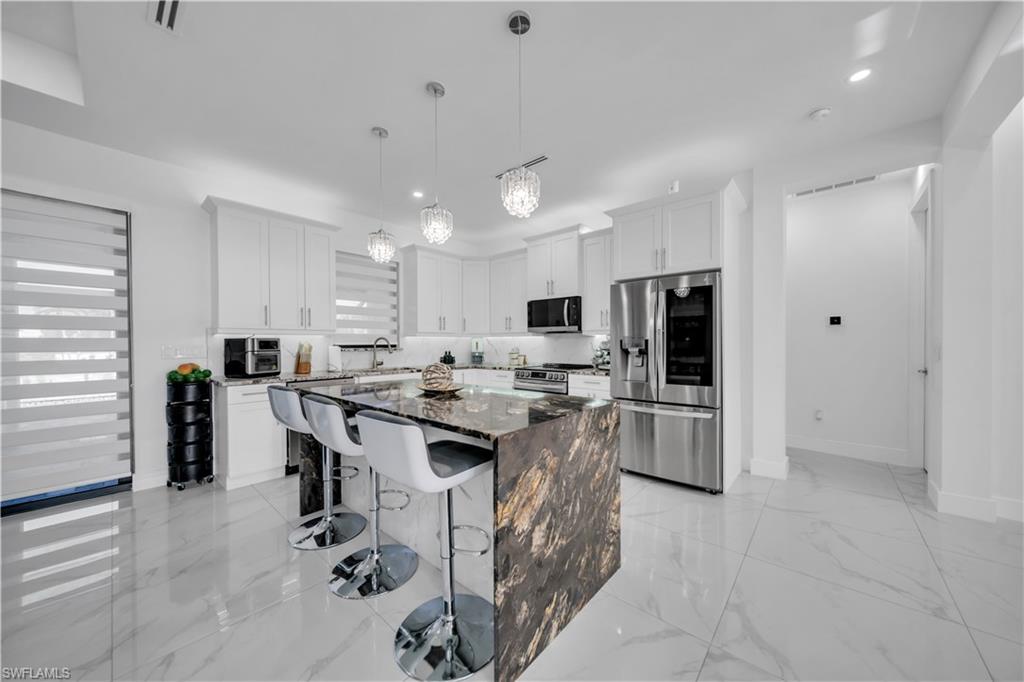 Gourmet kitchen with a waterfall island, integrated stainless steel appliances, white shaker cabinetry, pendant lighting, and polished tile flooring
