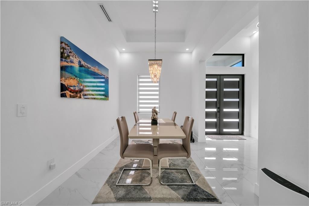 Porcelain tile flooring, modern double entry doors with frosted glass panels, tray ceiling, recessed lighting, and a contemporary linear chandelier