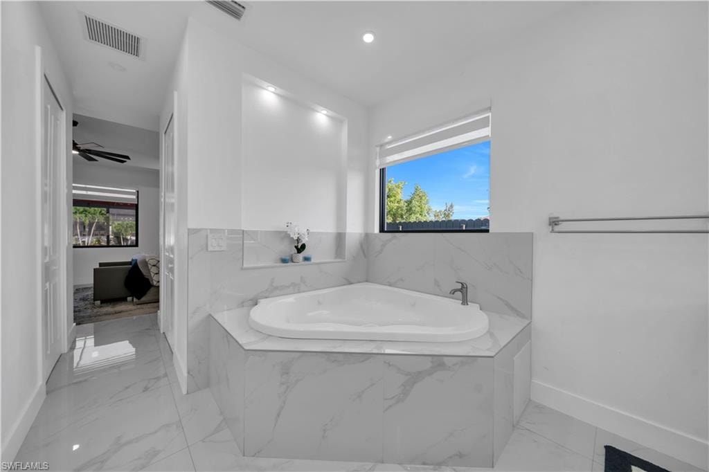 Corner soaking tub with a tiled surround, recessed wall niche, and an adjacent window with a roller shade