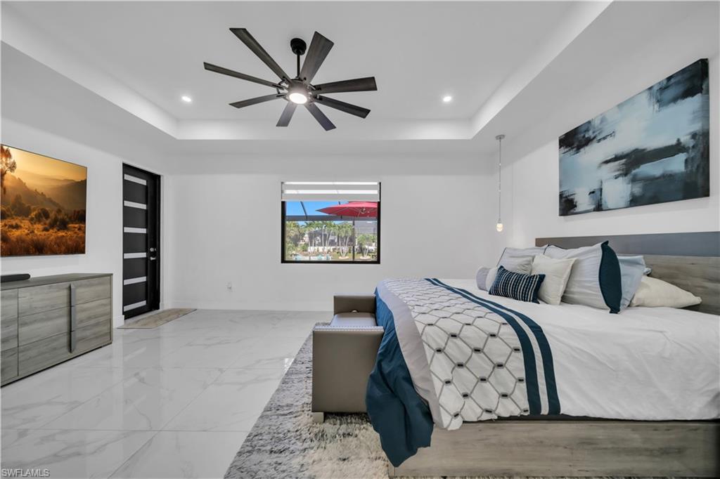 Spacious primary bedroom showcasing polished stone-finish flooring, a tray ceiling with recessed lighting, and a modern ceiling fan with brushed metal finish