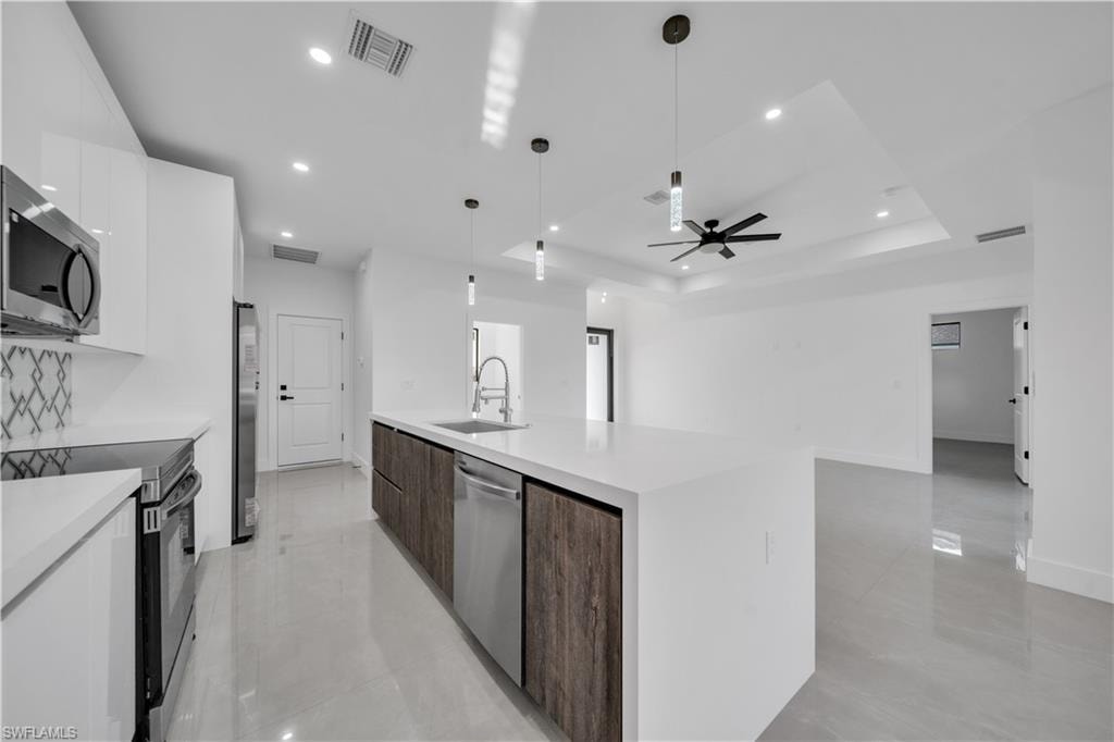 Modern kitchen featuring white cabinetry, stainless steel appliances, a center island with sink, contemporary pendant lighting, and recessed ceiling lights