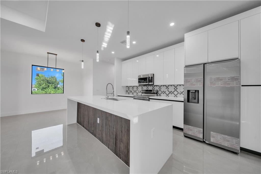 Kitchen island with waterfall countertop, pendant lighting, built-in stainless steel appliances, and a geometric pattern tile backsplash