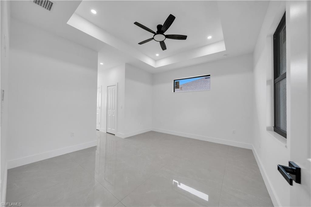 Tray ceiling with recessed lighting, black ceiling fan, large format tile flooring, and white interior doors