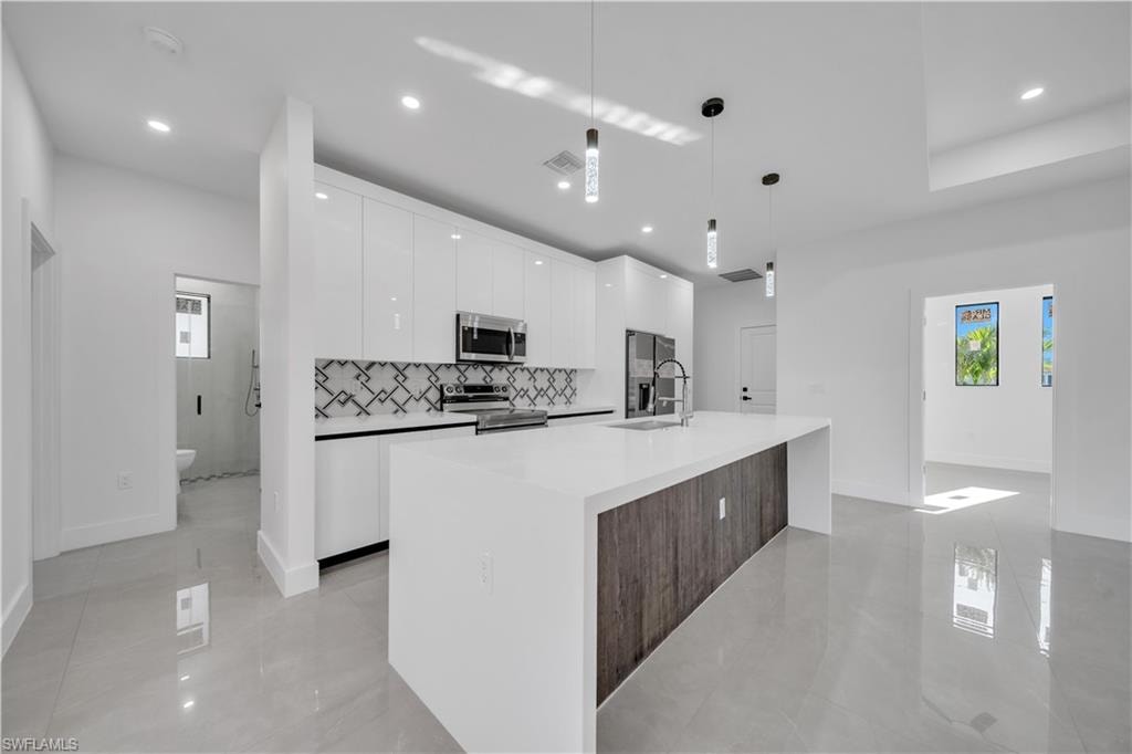 Modern kitchen featuring a large island with white countertop, sleek white cabinetry, stainless steel appliances, and a geometric tile backsplash