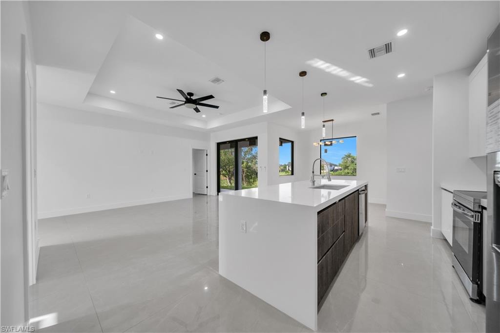 Contemporary kitchen featuring white flat-panel cabinetry, stainless steel appliances, a patterned tile backsplash, and a large center island with a stainless steel sink